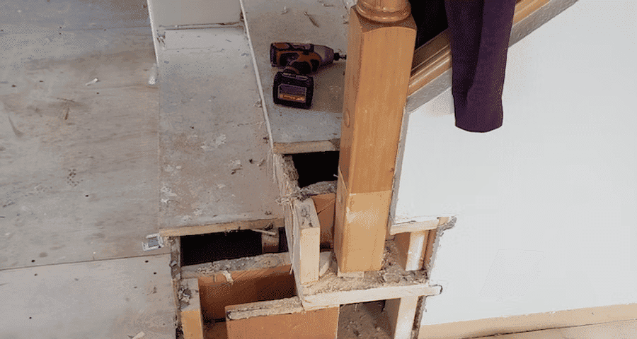 Staircase renovation showing exposed wood framing and tools on a dusty floor.