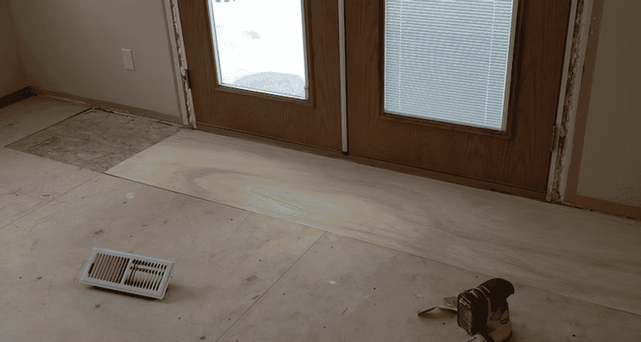 Interior renovation in progress with unfinished flooring and tools near double glass doors.