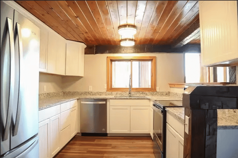 Modern kitchen with wooden ceiling, granite countertops, stainless steel appliances, and natural light.