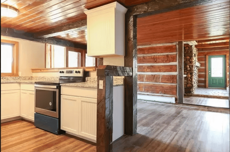Modern kitchen with white cabinetry, granite countertops, and a view of a rustic wooden living area.