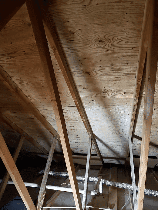 Exposed wooden beams and plywood ceiling in an unfinished attic space.