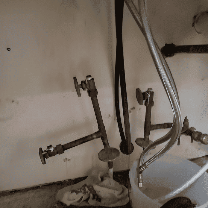 Plumbing pipes and fittings under a sink with visible wear and tear.