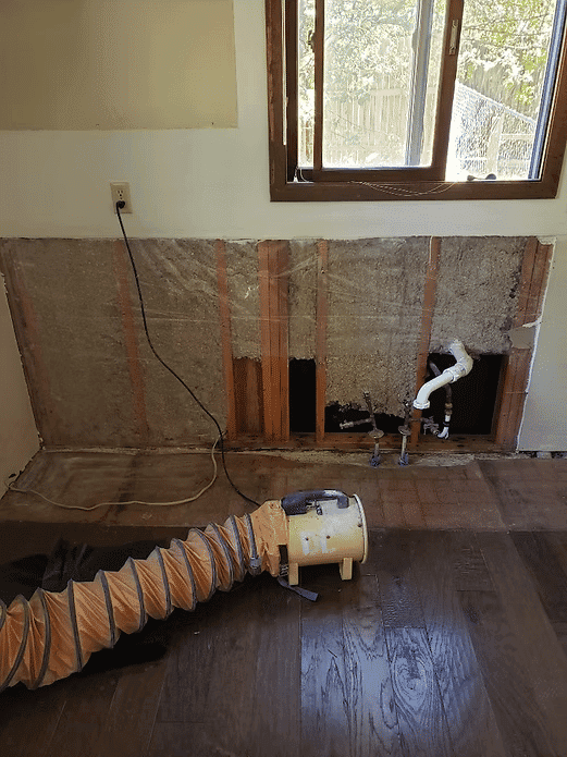 Exposed wall with plumbing and a vacuum cleaner for home renovation repair.