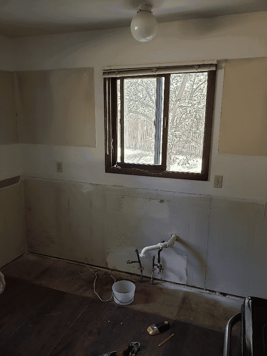 Renovating a kitchen with unfinished walls and a window overlooking a backyard.