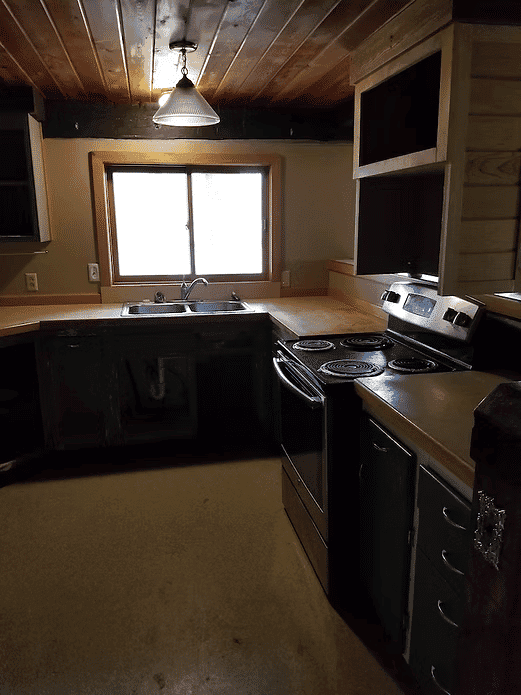 Rustic kitchen with wooden ceiling, modern stove, and sink under a bright window.