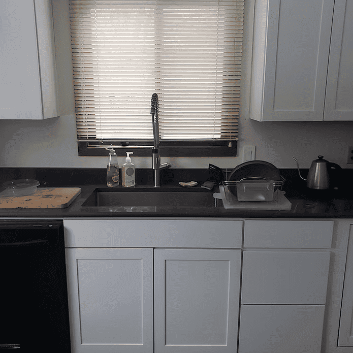 Modern kitchen featuring white cabinets, a black countertop, and a sink with a window.