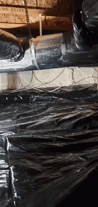 Ventilation ducting in a basement with black plastic sheeting covering the ground.