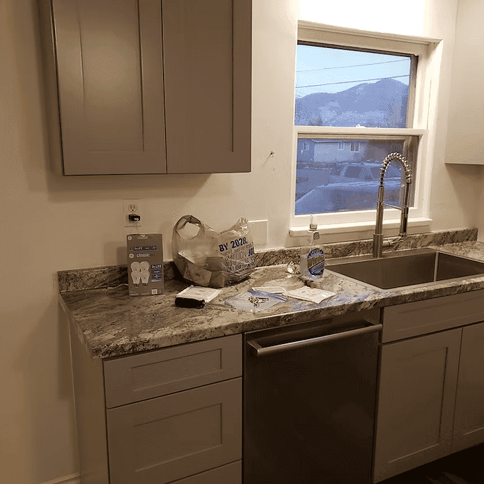 Modern kitchen with granite countertop, stainless steel sink, and gray cabinets. Natural light from window.