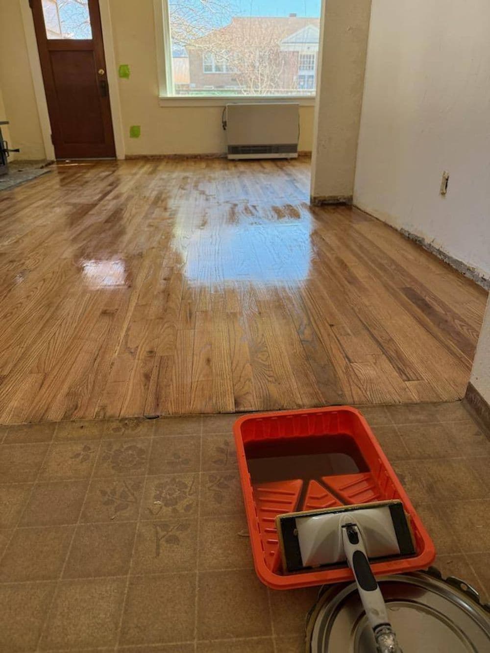Refinished hardwood floor with a paint roller and tray in a home interior.