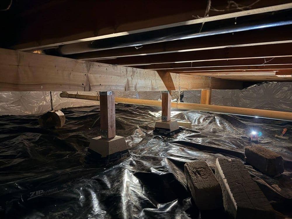 Crawl space with foundation piers, concrete blocks, and black plastic sheeting for moisture barrier.