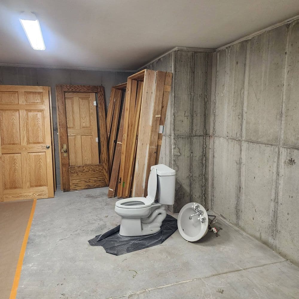 Toilet in unfinished basement with wooden doors and construction materials nearby.
