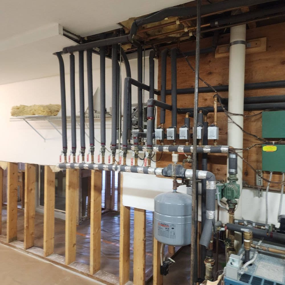 Complex plumbing system with pipes, gauges, and valves in a partially finished basement.